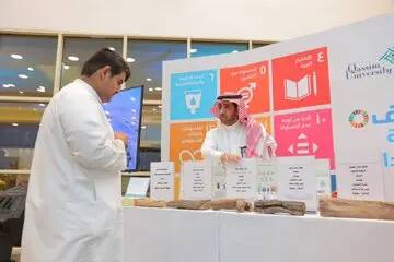 رجل ألتان يرتديان الزي السعودي التقليدي، متمثلاً في الشماغ أو الغترة السعودية، عند الجناح يحتوي على عروض مُعنونة، حيث يعرضان تقريراً حول الهدف الثاني عشر. ينصح بخلفهما ملصقات توعوية ولوحة تحمل اسم جامعة القصيم. يتولى تفسير محتوى التقرير بينما يقوم الآخرون بمتابعة ما يُعرض على الجدول.
