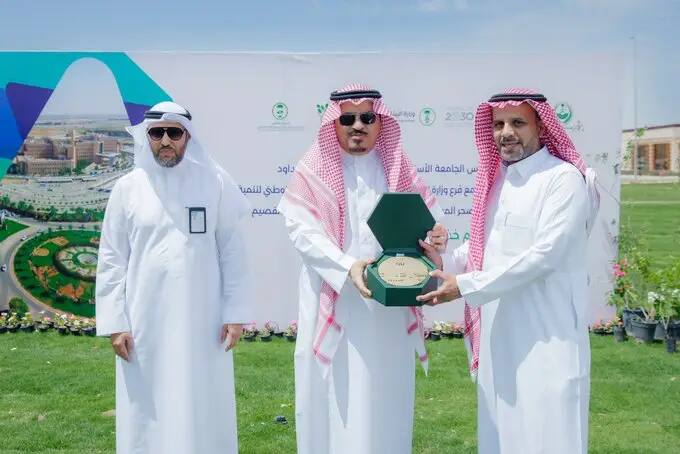 إليك ثلاثة رجال تولي الزي السعودي الأصلي، الرجل في المنتصف وهو يسلم درعاً تكريمياً الأخضر للرجل الواقف على يمينه، وذلك احتفاءً بالهدف الثاني عشر. ينصح في الخلفية بتحمل شعار بعض الزهور.