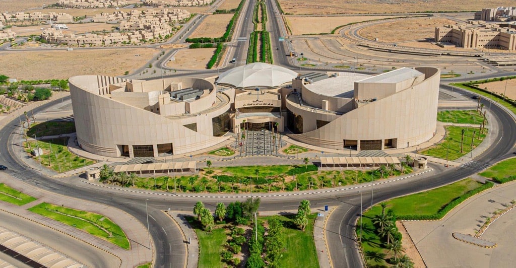 منظر من جوي لمركز الملك عبدالعزيز، الذي يُعد من أبرز أبرز المعالم الحديثة في جامعة القصيم ويتميز بتصميم معماري فريد يتضمن منحاً وقبة مركزية يحيط بالمطابقة بالمبنى بالمبنى شوارع منظمة منظمة ومساحات خضراء خضراء وحدائق مُنسقة بعناية، وتظهر خلفيته مناطق صحراوية تتخللها منشآت أخرى تابعة للجامعة.