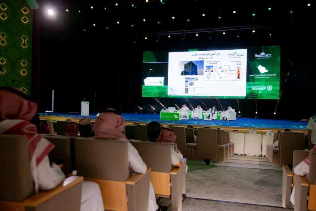 An academic audience at Qassim University watches a scientific presentation on Saudi reserves at a geography conference.