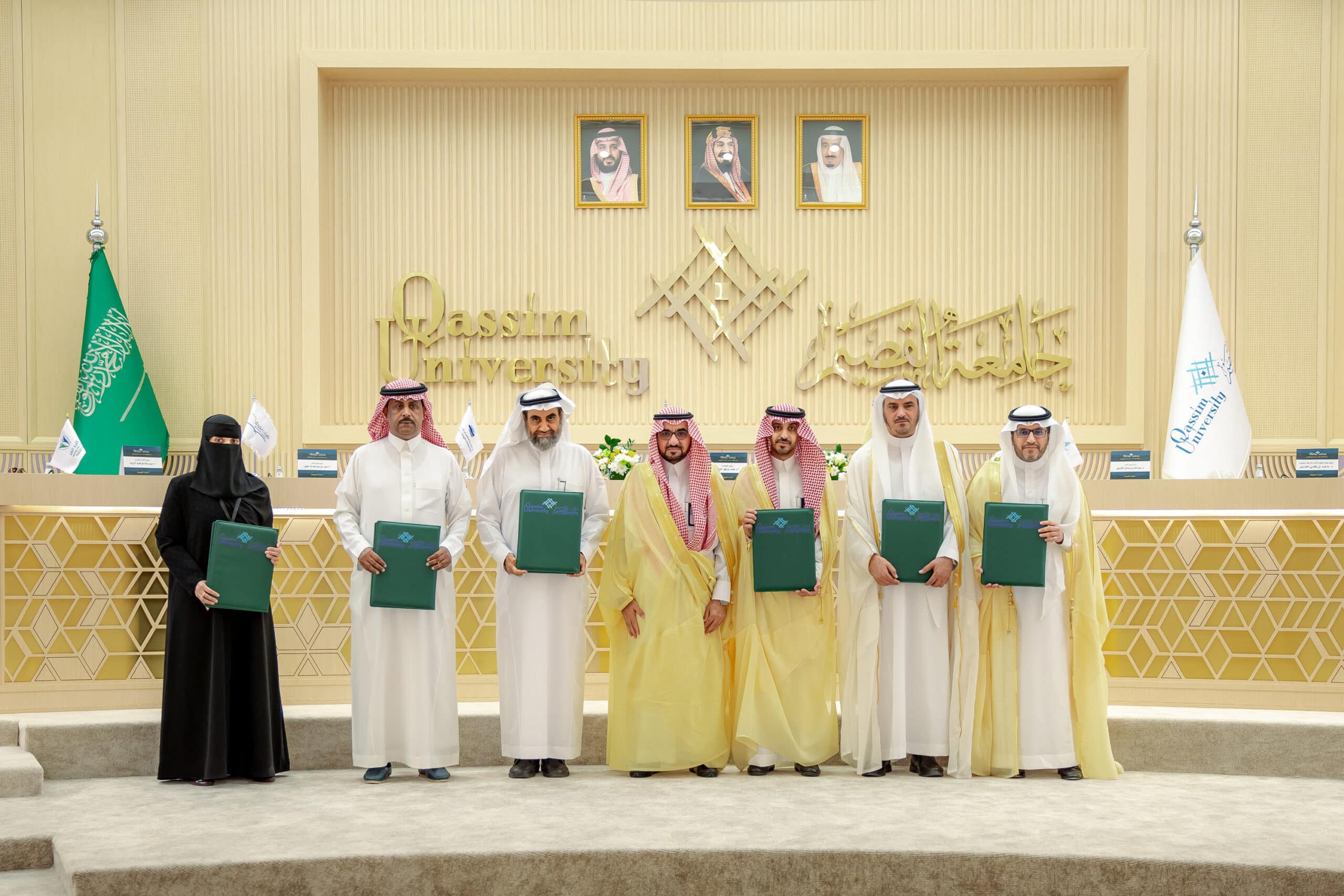 Participants honored at Qassim University amidst national flags, photos and images at an official academic event.