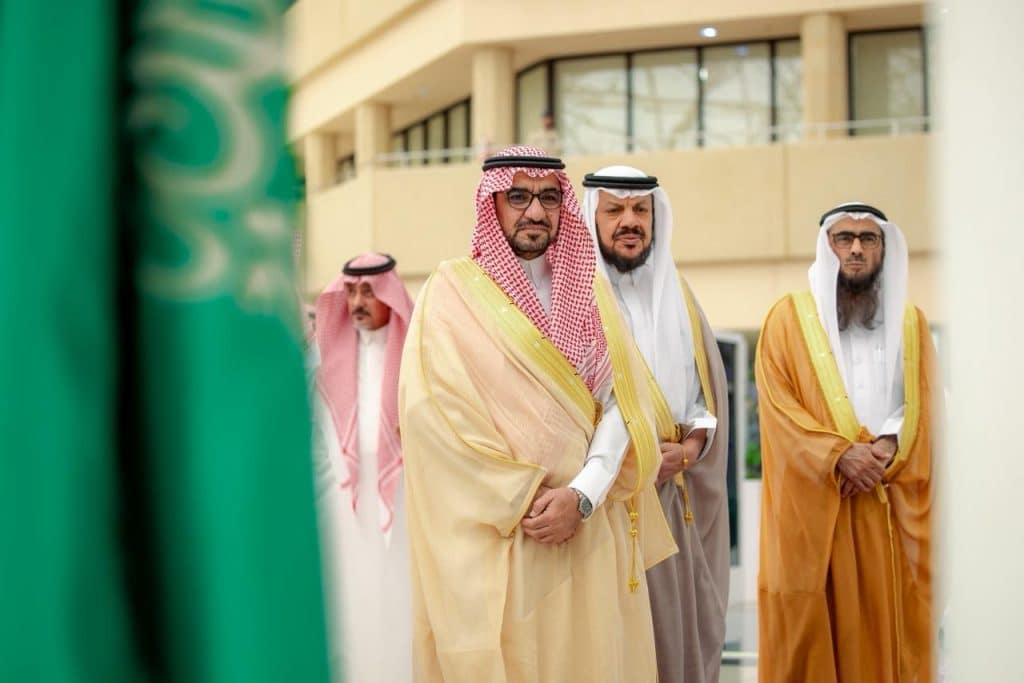 اجتماع أكاديمي في جامعة القصيم يظهر علم المملكة ووثائق على طاولة داخل مبنى حديث.