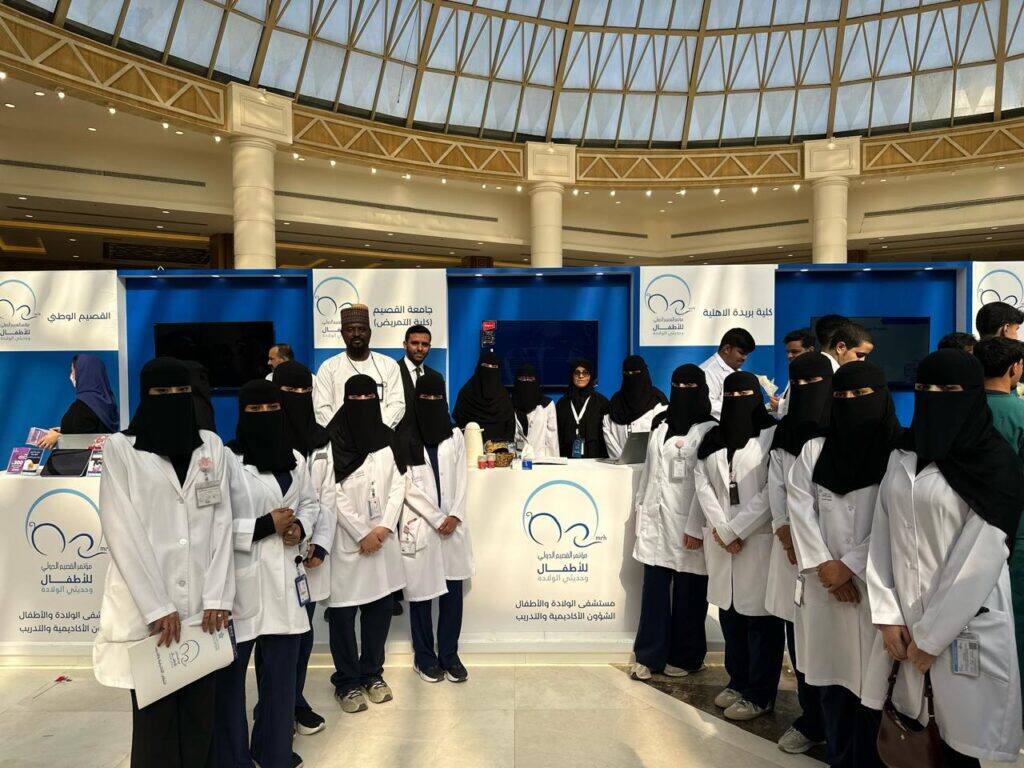 فريق جامعة القصيم أمام جناح مؤتمر أكاديمي، في قاعة داخلية مضيئة.