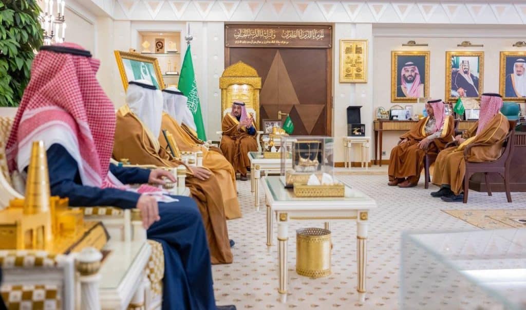 An official meeting in a Qassim University auditorium decorated with Saudi and Islamic touches and state flags.