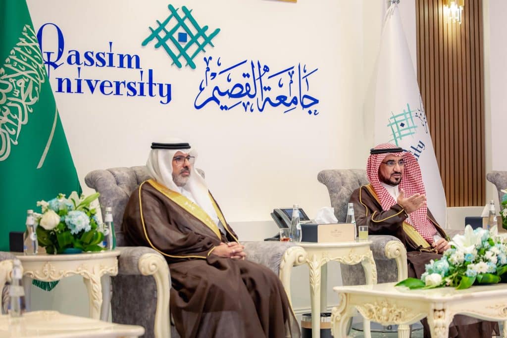 A formal session at Qassim University attended by Saudi dignitaries, with the city's logo prominent in the background.