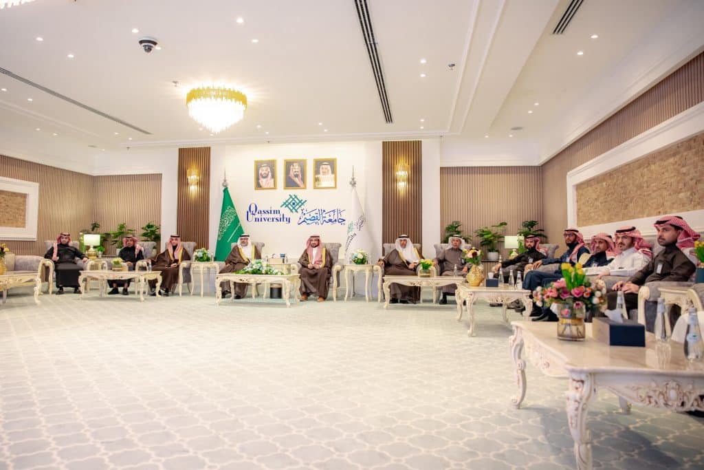 An official meeting of Qassim Medical University in a hall decorated with flags and photos in an academic context.