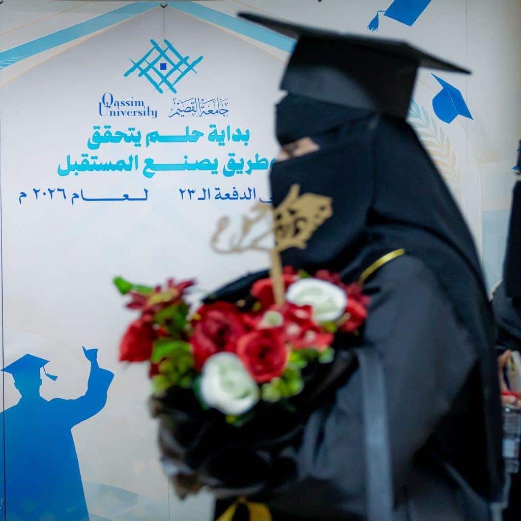 A graduate celebrates her graduation in front of the Qassim University logo at the 2023-2024 graduation ceremonies.