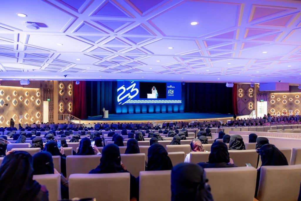 An official graduation ceremony at Qassim University with the event's logo and the 23rd class displayed on the screen.