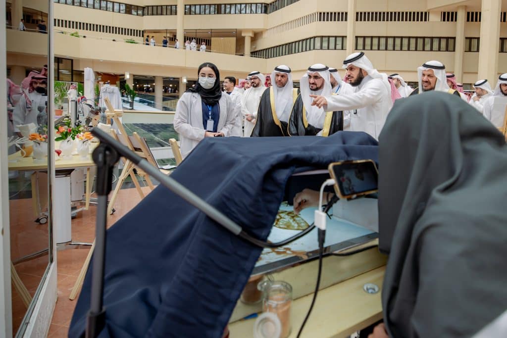 عرض علمي بجامعة القصيم حيث يشاهد الحضور تجربة الحضور مخبرية توثق بهواتفهم الذكية.