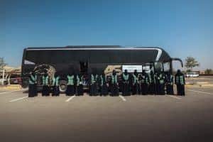 An academic gathering of Qassim University female students in front of a university bus in a clear courtyard.