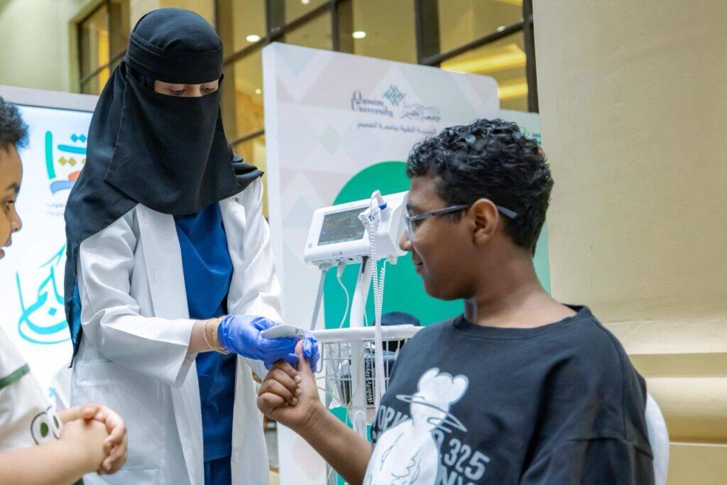 فحص ضغط دم لطفل بجهاز رقمي في ركن صحي ضمن فعاليات جامعة القصيم.