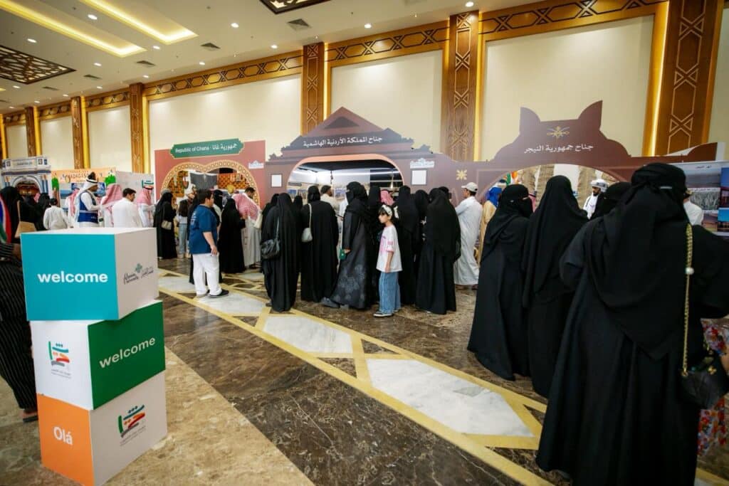 A crowd in a closed hall at Qassim University participates in an event with a Saudi Islamic identity.