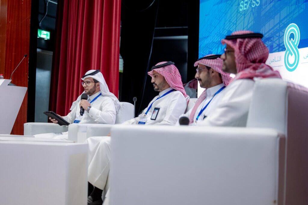 ندوة علمية بجامعة القصيم ضمن الملتقى الهندسي، أحد المشاركين يتحدث أمام شاشة الحدث.