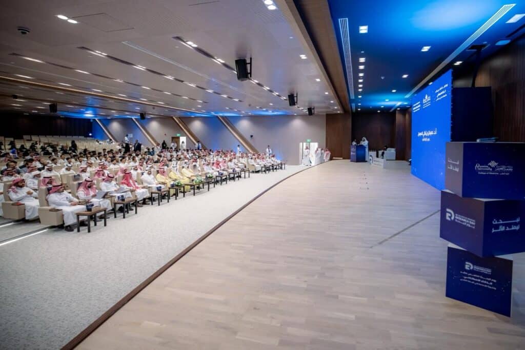 ملتقى يوم البحث في قاعة حديثة بجامعة رئيس الجامعة يخاطب الحضور من منصة العرض.