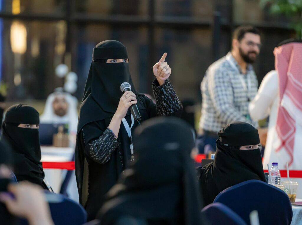 A female member participates in an academic event at Qassim University within the Innovators Forum.
