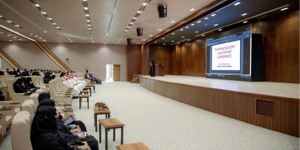 Qassim University lecture hall hosts a scientific presentation on pharmacy and dietary supplements.